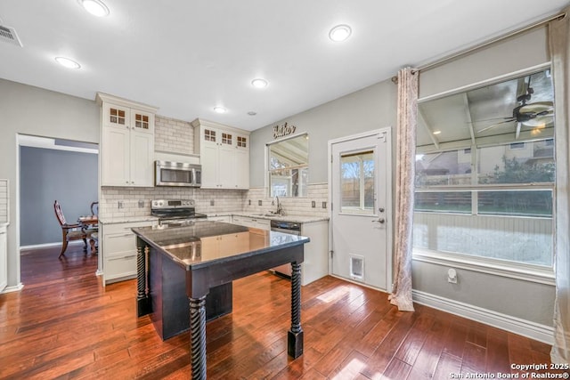 kitchen with stainless steel appliances, glass insert cabinets, light stone counters, and tasteful backsplash