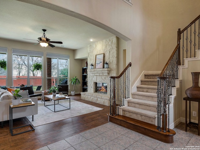 living area featuring ceiling fan, a fireplace, wood finished floors, baseboards, and stairway