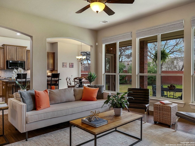 living area with light wood-style flooring, visible vents, arched walkways, and ceiling fan with notable chandelier