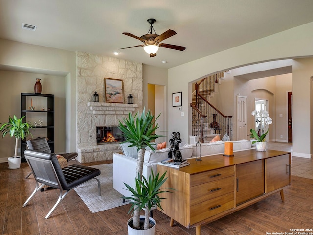 living room featuring arched walkways, visible vents, a stone fireplace, wood finished floors, and stairs