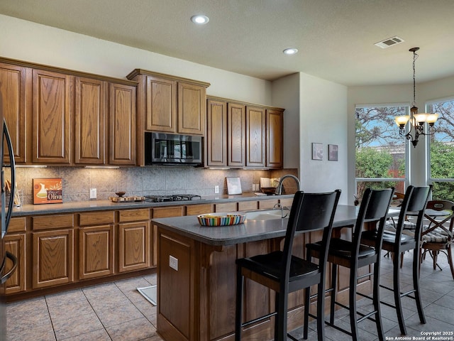 kitchen featuring brown cabinets, stainless steel appliances, visible vents, decorative backsplash, and a kitchen breakfast bar