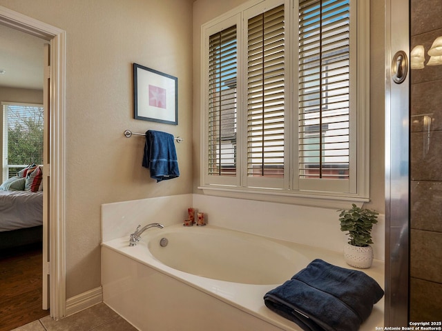 ensuite bathroom with a garden tub, baseboards, tile patterned flooring, and connected bathroom