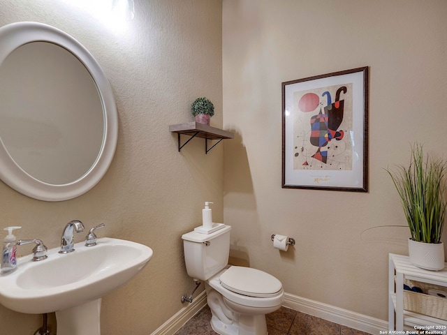 half bath featuring baseboards, a sink, toilet, and tile patterned floors