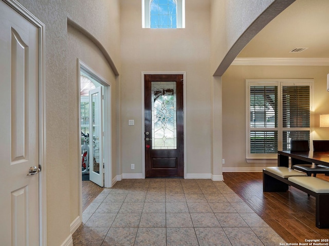 foyer entrance featuring arched walkways, visible vents, ornamental molding, tile patterned flooring, and baseboards