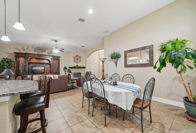 dining space featuring arched walkways, a fireplace, light tile patterned floors, visible vents, and ceiling fan