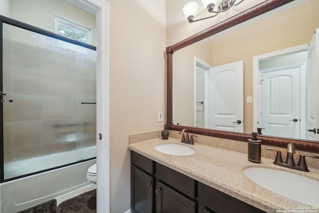 full bathroom featuring bath / shower combo with glass door, a sink, toilet, and double vanity