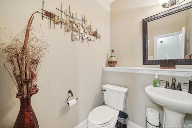 half bathroom with toilet, baseboards, and a sink