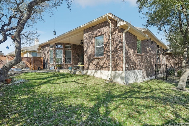 back of property featuring ceiling fan, fence, a lawn, and brick siding