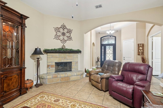 tiled living room with arched walkways, a stone fireplace, visible vents, and baseboards