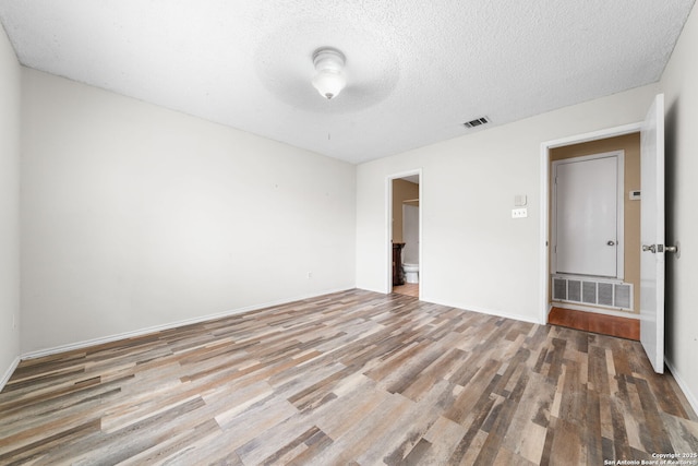 empty room featuring baseboards, a textured ceiling, visible vents, and wood finished floors