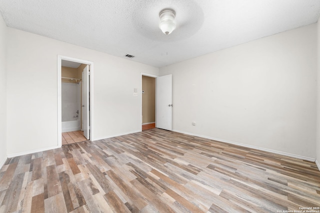 unfurnished bedroom featuring light wood-type flooring, visible vents, a textured ceiling, and baseboards