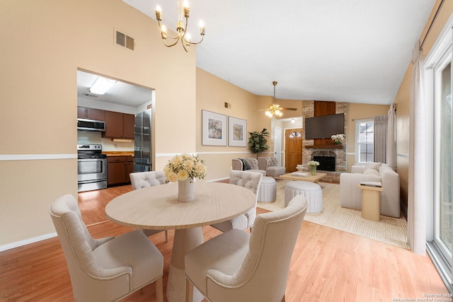 dining space with a fireplace, visible vents, light wood-style floors, baseboards, and ceiling fan with notable chandelier