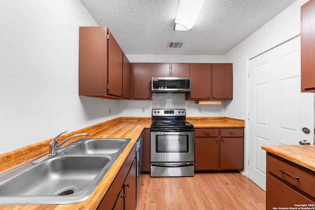 kitchen with a textured ceiling, a sink, visible vents, light wood-style floors, and appliances with stainless steel finishes