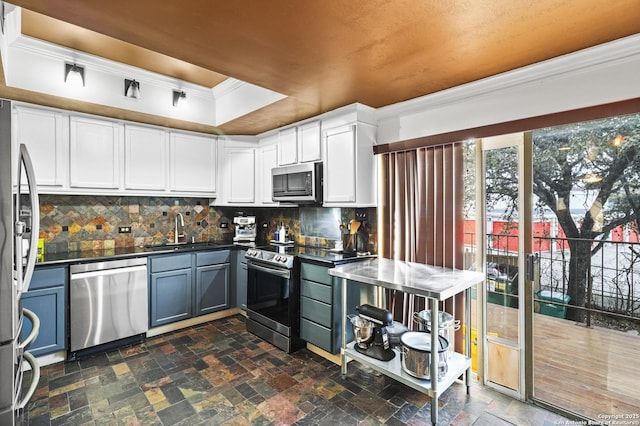 kitchen featuring a raised ceiling, appliances with stainless steel finishes, stone finish flooring, white cabinetry, and a sink