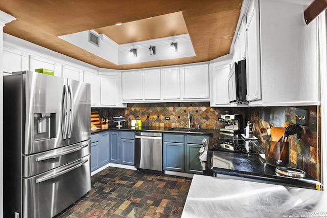 kitchen with a sink, appliances with stainless steel finishes, decorative backsplash, a tray ceiling, and dark countertops