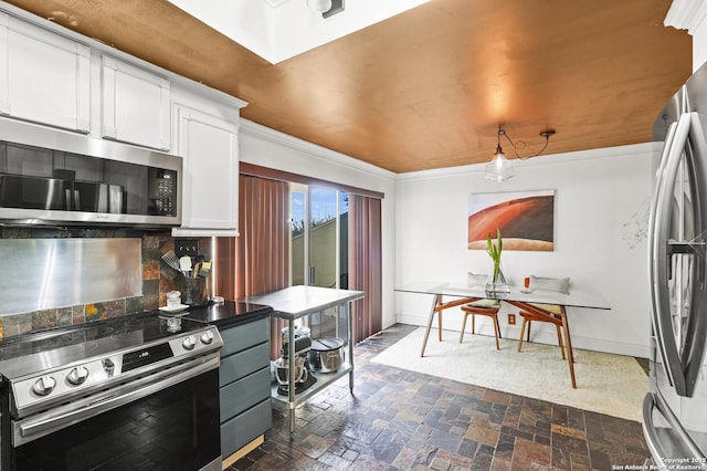 kitchen with appliances with stainless steel finishes, ornamental molding, stone finish flooring, white cabinetry, and baseboards