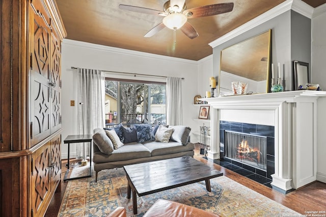 living area featuring baseboards, a ceiling fan, wood finished floors, crown molding, and a fireplace