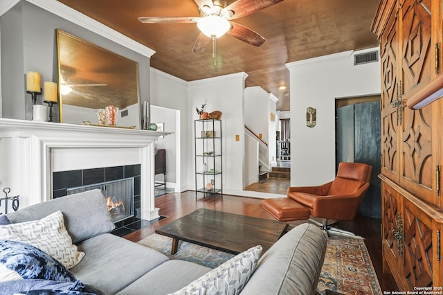 living room with crown molding, visible vents, a tiled fireplace, wood finished floors, and stairs