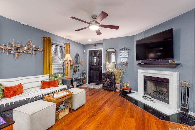 living room featuring ceiling fan, a fireplace with raised hearth, and wood finished floors