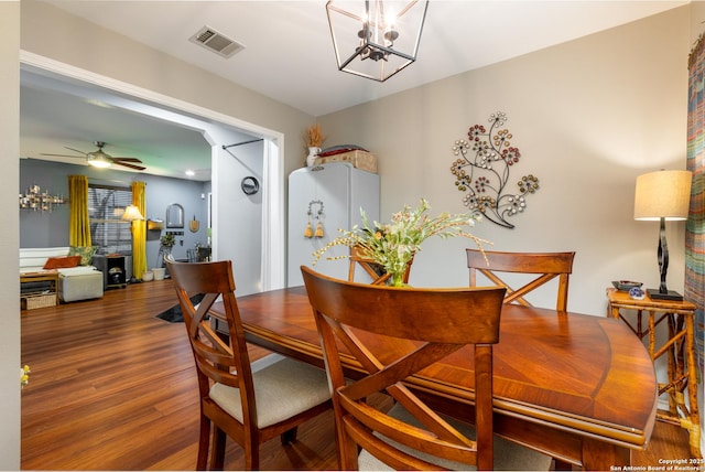 dining space with ceiling fan with notable chandelier, visible vents, and wood finished floors