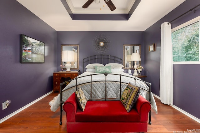 bedroom with ornamental molding, a raised ceiling, baseboards, and wood finished floors