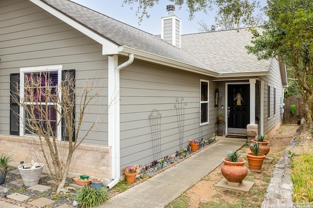 view of exterior entry featuring a shingled roof and a chimney