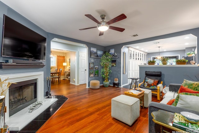 living area featuring visible vents, a fireplace with raised hearth, ceiling fan, wood finished floors, and baseboards