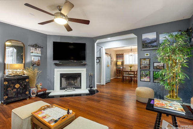 living area featuring a ceiling fan, a fireplace with raised hearth, baseboards, and wood finished floors