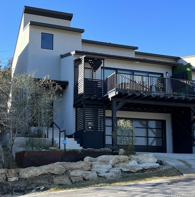 view of front facade with stucco siding, concrete driveway, stairway, an attached garage, and a wooden deck