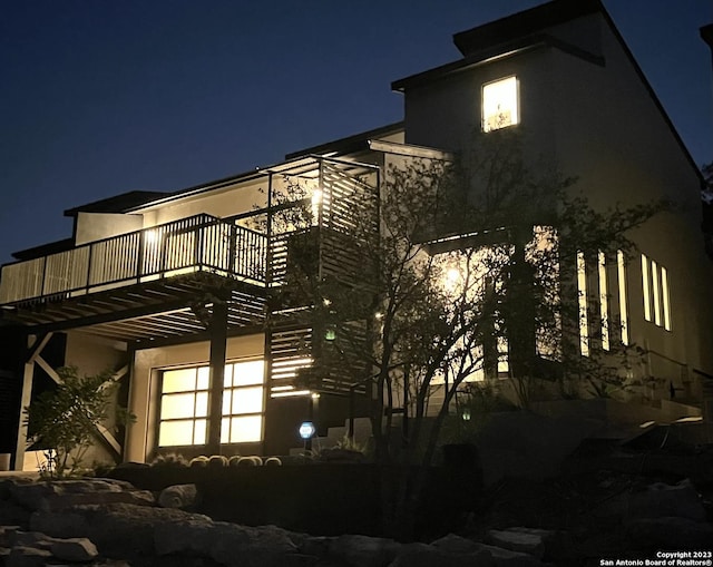 property exterior at night featuring a balcony and stucco siding