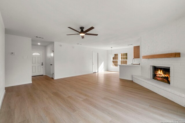 unfurnished living room with a ceiling fan, visible vents, a fireplace, and light wood finished floors