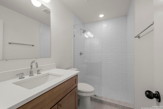 bathroom with visible vents, a tile shower, vanity, and toilet