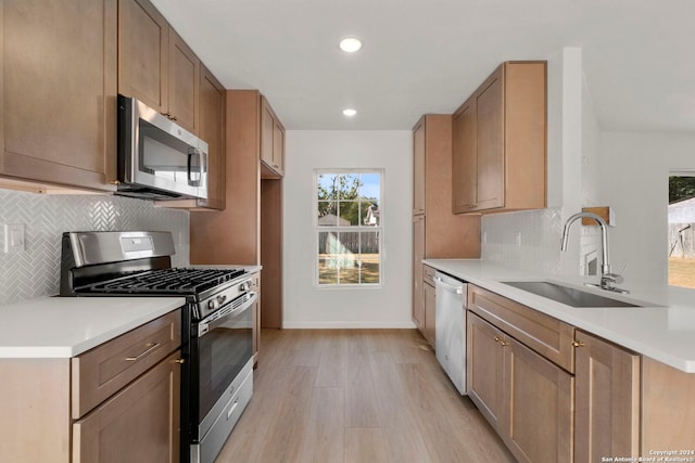 kitchen featuring a sink, light countertops, appliances with stainless steel finishes, decorative backsplash, and light wood finished floors