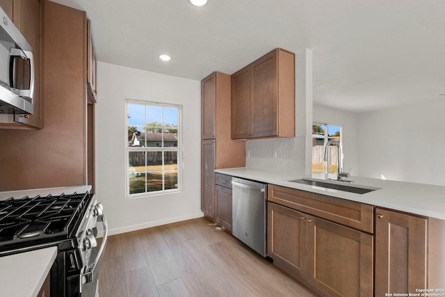 kitchen with appliances with stainless steel finishes, light countertops, a sink, and light wood-style flooring