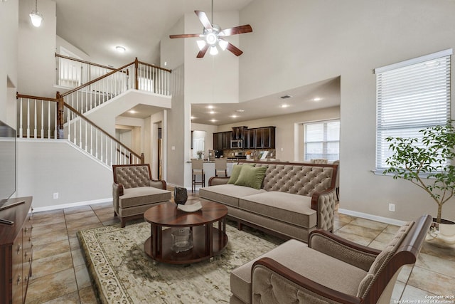 living room featuring light tile patterned floors, ceiling fan, baseboards, and stairs