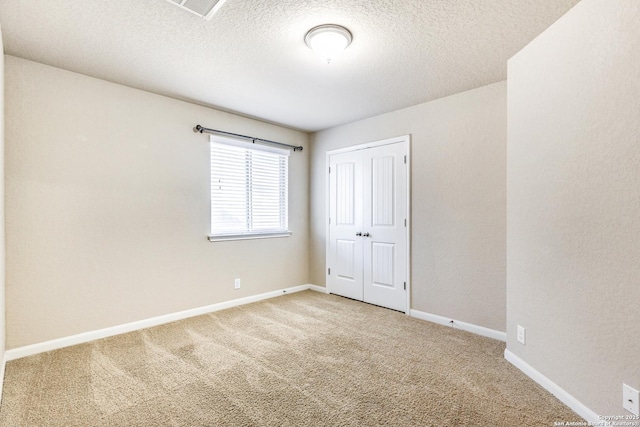 unfurnished bedroom with a textured ceiling, light carpet, visible vents, baseboards, and a closet