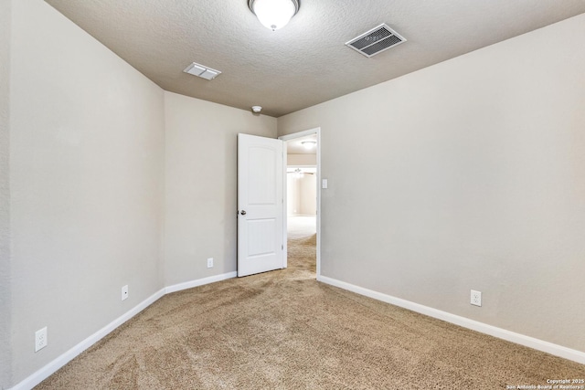 carpeted spare room featuring a textured ceiling, visible vents, and baseboards