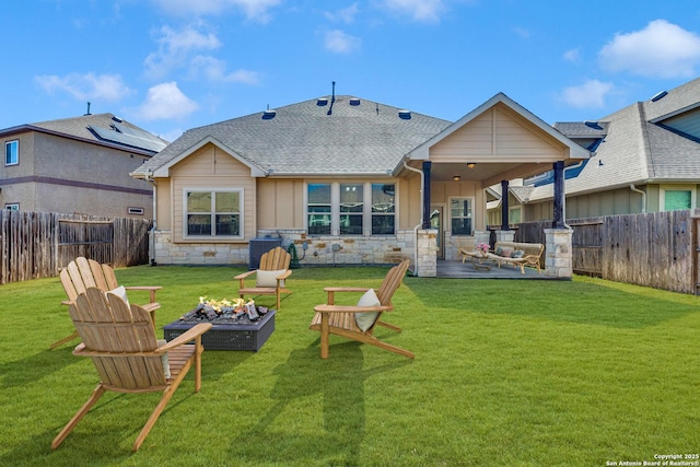 back of house featuring stone siding, a fenced backyard, a fire pit, and a lawn