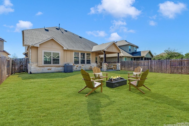 back of property featuring central air condition unit, a shingled roof, a lawn, stone siding, and a fire pit