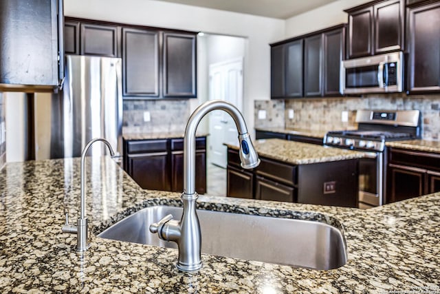 kitchen with decorative backsplash, light stone counters, stainless steel appliances, dark brown cabinets, and a sink