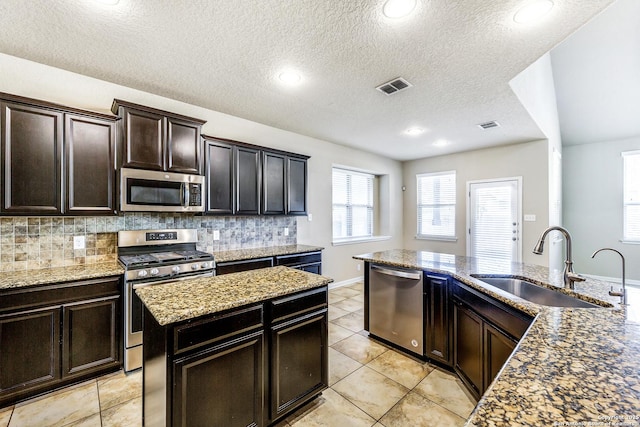 kitchen with tasteful backsplash, visible vents, light stone counters, appliances with stainless steel finishes, and a sink