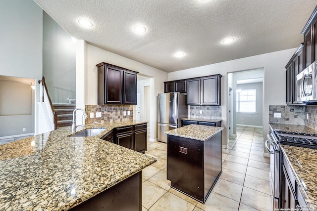 kitchen with appliances with stainless steel finishes, light stone counters, a center island, dark brown cabinets, and a sink