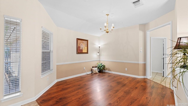 empty room featuring a wealth of natural light, visible vents, an inviting chandelier, and wood finished floors