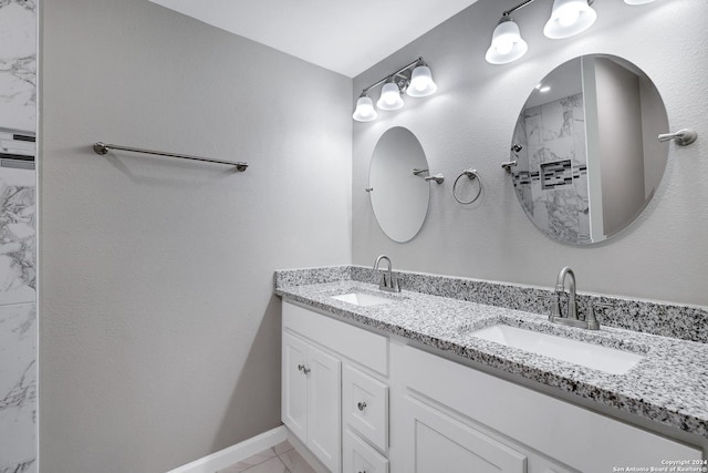 bathroom featuring a tile shower, double vanity, a sink, and baseboards