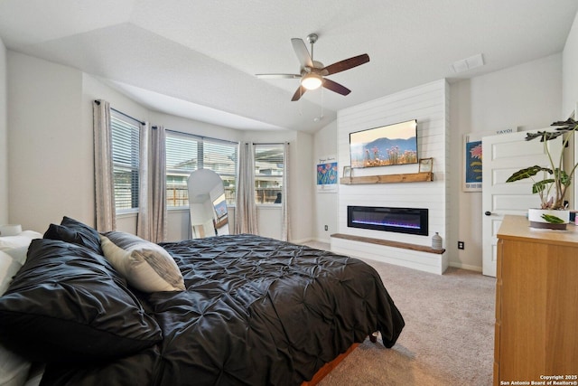 carpeted bedroom with lofted ceiling, a glass covered fireplace, visible vents, and a ceiling fan