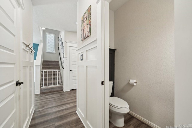 bathroom featuring baseboards, a textured wall, toilet, and wood finished floors