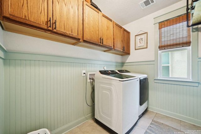 clothes washing area featuring cabinet space, visible vents, wainscoting, independent washer and dryer, and light tile patterned flooring