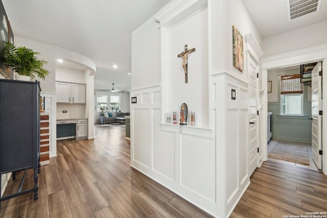 hall featuring recessed lighting, a decorative wall, dark wood-style flooring, visible vents, and wainscoting