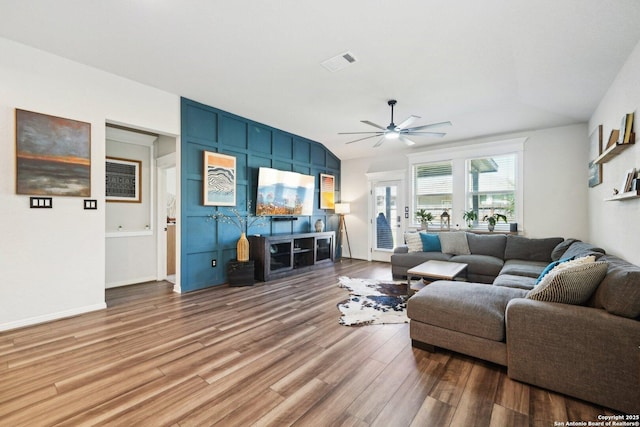 living room with lofted ceiling, wood finished floors, visible vents, baseboards, and a ceiling fan