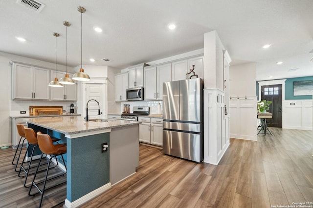 kitchen with stainless steel appliances, visible vents, a sink, wood finished floors, and a kitchen breakfast bar